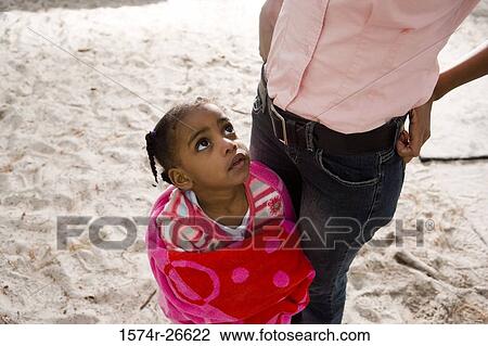 Stock Image - Girl in towel standing by her mother on the sand. Fotosearch
