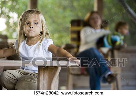 Girl sitting by a table while mother holding her son in the background View Large Photo Image Stock Image - Girl sitting by a table while mother holding her son in the background. Fotosearch