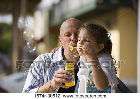 Girl sitting with her father and blowing bubbles through a bubble blower View Large Photo Image Stock Image - Girl sitting with her father and blowing bubbles through a bubble blower. Fotosearch