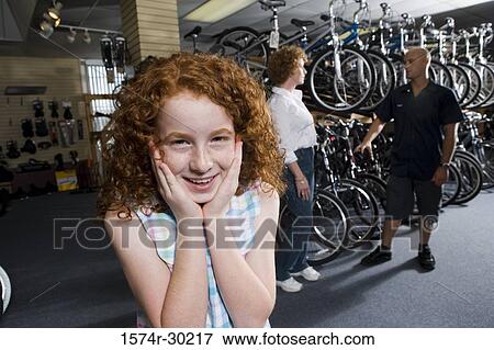 Stock Photo - Girl smiling while her mother in conversation with cycle owner in a bicycle shop. Fotosearch