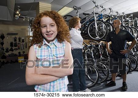 Stock Photography - Girl smiling while her mother in conversation with cycle owner in a bicycle shop. Fotosearch