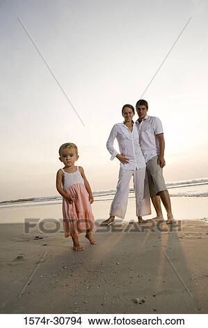 Picture - Girl standing on the beach with parents in the background. Fotosearch