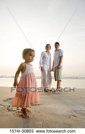 Girl standing on the beach with parents in the background View Large Photo Image Stock Image - Girl standing on the beach with parents in the background. Fotosearch