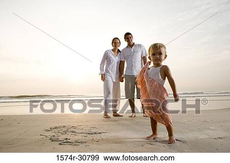 Girl standing on the beach with parents in the background View Large Photo Image Stock Photo - Girl standing on the beach with parents in the background. Fotosearch