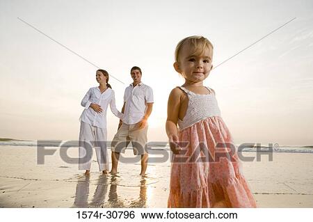 Girl standing on the beach with parents in the background View Large Photo Image Stock Photograph - Girl standing on the beach with parents in the background. Fotosearch