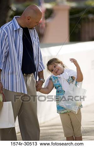 Girl with father holding shopping bags whiles walking on the street View Large Photo Image Stock Image - Girl with father holding shopping bags whiles walking on the street. Fotosearch