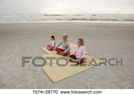 Stock Image - Grandmother exercising with daughter and granddaughter on a mat at the beach. Fotosearch