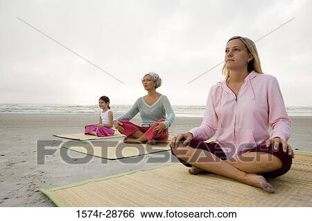 Stock Photograph - Grandmother exercising with daughter and granddaughter on a mat at the beach. Fotosearch