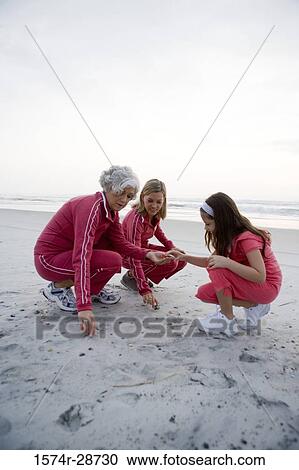 Stock Image - Grandmother with her daughter and granddaughter collecting stones at the beach. Fotosearch