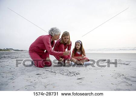 Stock Image - Grandmother with her daughter and granddaughter collecting stones at the beach. Fotosearch