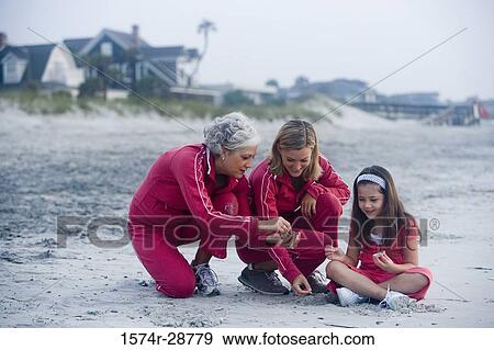 Stock Photo - Grandmother with her daughter and granddaughter collecting stones at the beach. Fotosearch