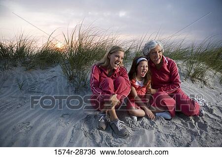 Stock Photograph - Grandmother with her daughter and granddaughter sitting at the beach. Fotosearch