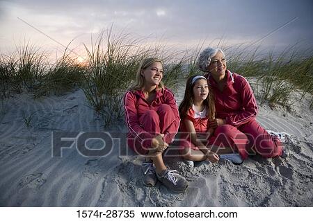 Stock Photography - Grandmother with her daughter and granddaughter sitting at the beach. Fotosearch