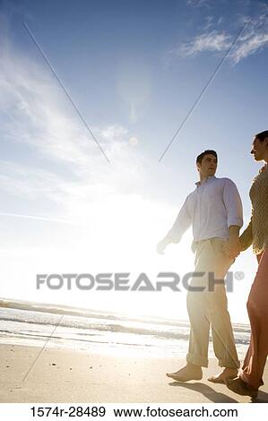 Stock Photo - Low angle view of couple holding hands and walking on a beach. Fotosearch
