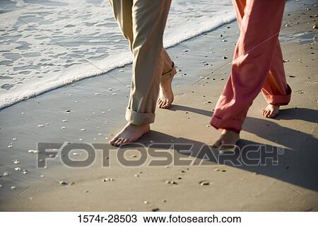 Low section of a couple walking on a beach View Large Photo Image Stock Image - Low section of a couple walking on a beach. Fotosearch