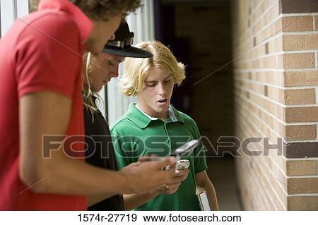 Male students text messaging on mobile phone in corridor View Large Photo Image Stock Photo - Male students text messaging on mobile phone in corridor. Fotosearch