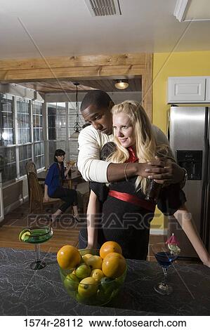Man embracing woman in domestic kitchen while their friends sitting in background View Large Photo Image Stock Image - Man embracing woman in domestic kitchen while their friends sitting in background. Fotosearch
