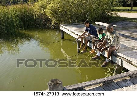 Stock Image - Man fishing with his son and friend on jetty. Fotosearch