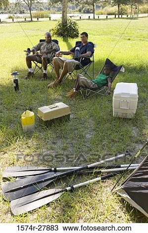 Stock Image - Man relaxing with his friend and son on chair at forest. Fotosearch