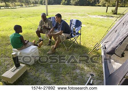 Stock Image - Man with his son and friend conversing by tent at forest. Fotosearch