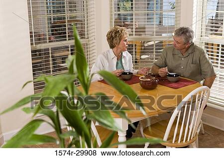 Mature couple sitting at breakfast table and having soup View Large Photo Image Stock Photo - Mature couple sitting at breakfast table and having soup. Fotosearch