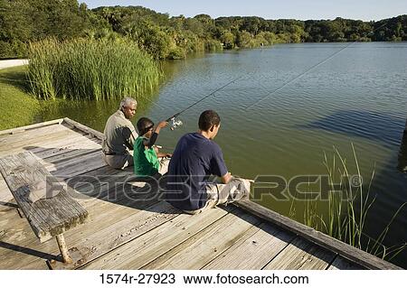 Stock Image - Mature man fishing with his son and friend on jetty. Fotosearch