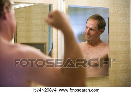 Picture - Mature man flexing muscles in the bathroom and looking at the bathroom mirror. Fotosearch