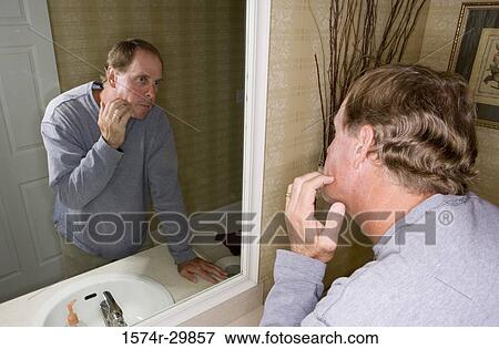 Mature man looking at his face in the bathroom mirror View Large Photo Image Stock Photo - Mature man looking at his face in the bathroom mirror. Fotosearch