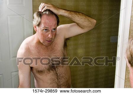 Stock Photo - Mature man looking at his face in the bathroom mirror. Fotosearch