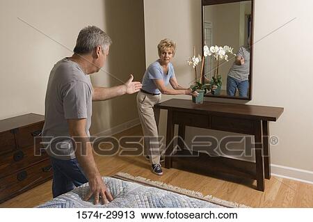Stock Image - Mature man pointing at mature woman holding a houseplant. Fotosearch
