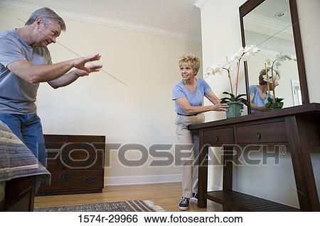 Stock Photograph - Mature man pointing at mature woman holding a houseplant. Fotosearch