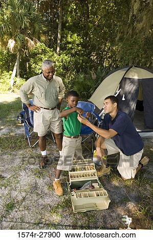 Stock Image - Mature man with his son and friend by tent at forest. Fotosearch