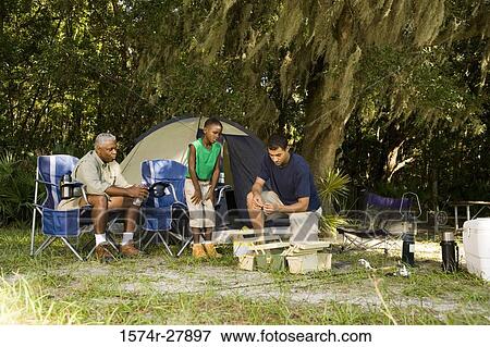 Stock Photo - Mature man with his son and friend by tent at forest. Fotosearch