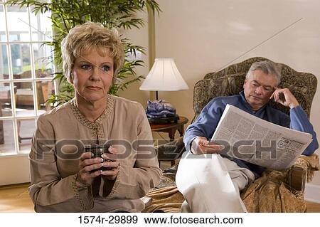 Stock Photo - Mature woman holding a cup while mature man sitting on a chair in background. Fotosearch