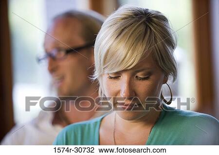 Stock Image - Mature woman looking down with husband in background. Fotosearch