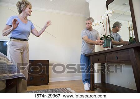 Mature woman pointing at mature man holding a houseplant View Large Photo Image Stock Photo - Mature woman pointing at mature man holding a houseplant. Fotosearch
