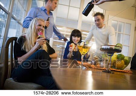 Stock Photograph - Men and women enjoying drinks in the dining room. Fotosearch