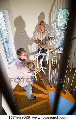 Mid adult couple carrying chairs on staircase View Large Photo Image Stock Photo - Mid adult couple carrying chairs on staircase. Fotosearch
