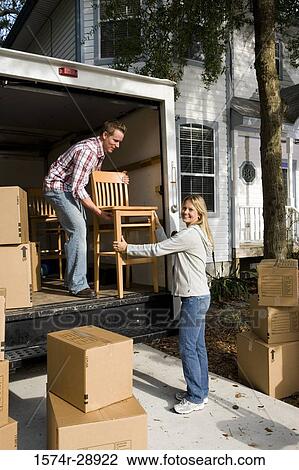 Stock Image - Mid adult couple unloading chairs and cardboard boxes from the moving van. Fotosearch
