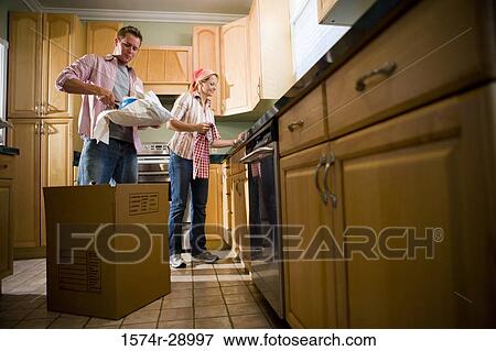 Mid adult couple unpacking cardboard box in the kitchen View Large Photo Image Stock Photo - Mid adult couple unpacking cardboard box in the kitchen. Fotosearch
