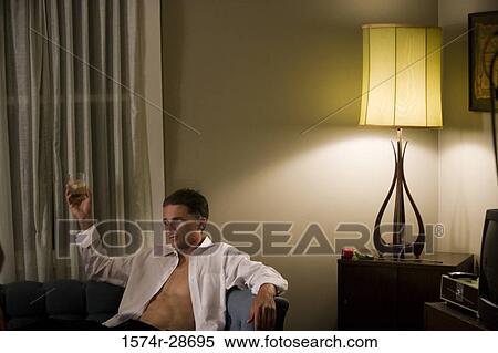 Mid adult man holding a glass while sitting on sofa View Large Photo Image Stock Photography - Mid adult man holding a glass while sitting on sofa. Fotosearch