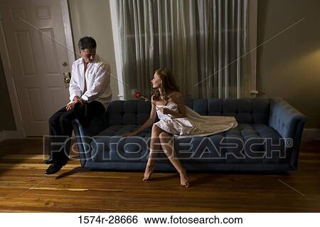 Stock Photograph - Mid adult man sitting by a young prostitute on sofa. Fotosearch
