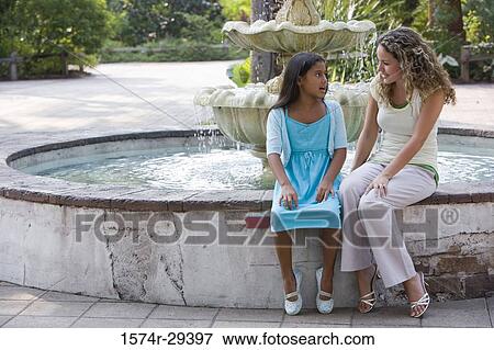 Stock Photo - Mother and daughter sitting together by water fountain. Fotosearch