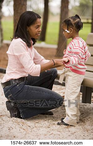 Mother dressing her daughter by bench at park View Large Photo Image Stock Photo - Mother dressing her daughter by bench at park. Fotosearch