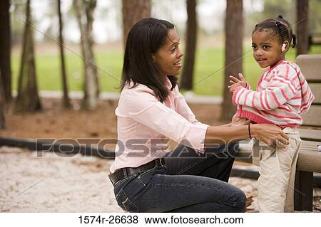 Mother dressing her daughter by bench at park View Large Photo Image Stock Photo - Mother dressing her daughter by bench at park. Fotosearch