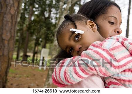 Mother embracing her daughter by a tree at park View Large Photo Image Stock Photo - Mother embracing her daughter by a tree at park. Fotosearch