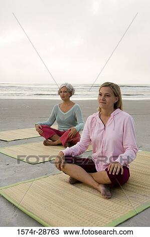 Stock Image - Mother exercising with daughter on a mat at the beach. Fotosearch