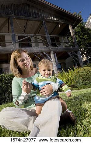 Stock Photo - Mother sitting with her son on grass in front of a house. Fotosearch