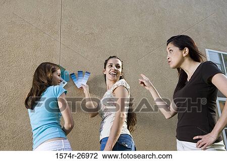 Stock Image - mother with her daughters holding color swatches against wall. Fotosearch