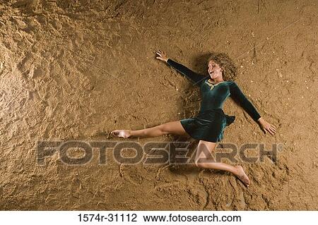 Stock Image - Overhead view of a cheerful young woman lying on sand. Fotosearch
